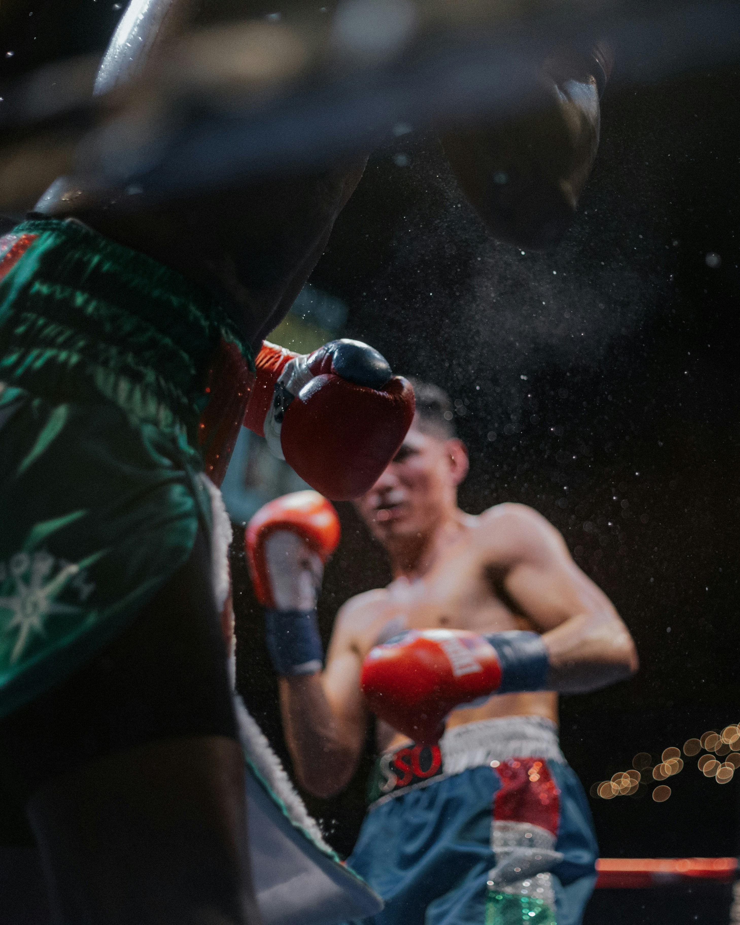 A boxer absorbing a glove to the head mid-round, spray of sweat caught in the light.