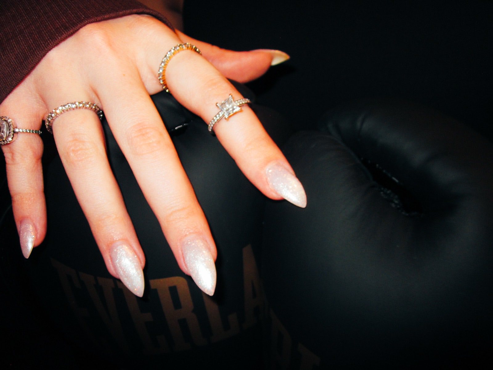 A manicured hand resting on a boxing glove — jewellery against black leather.