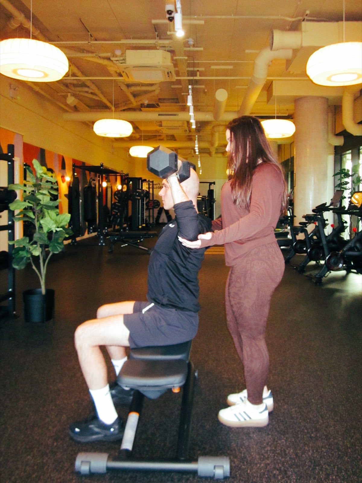 Maria Elena Cismarescu spotting a client through a seated dumbbell press.