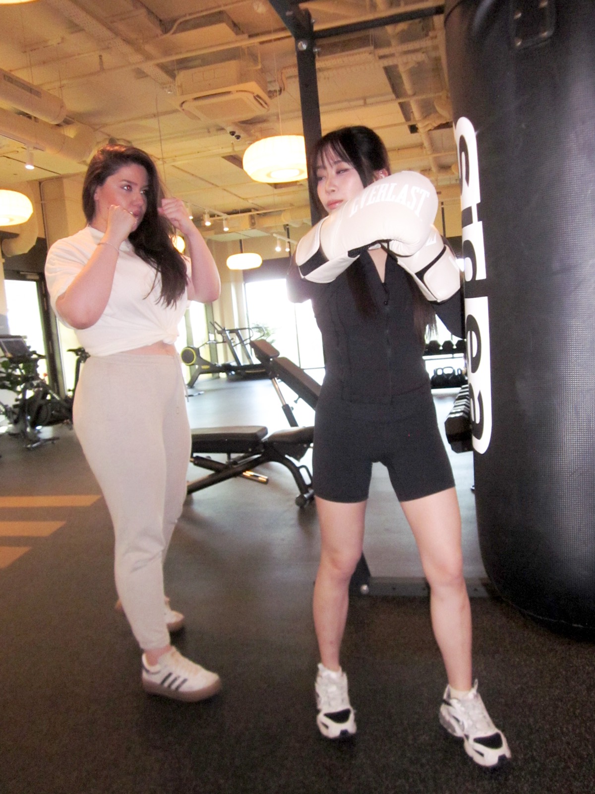 Maria Elena Cismarescu coaching a client's guard at the heavy bag in cream tailoring.