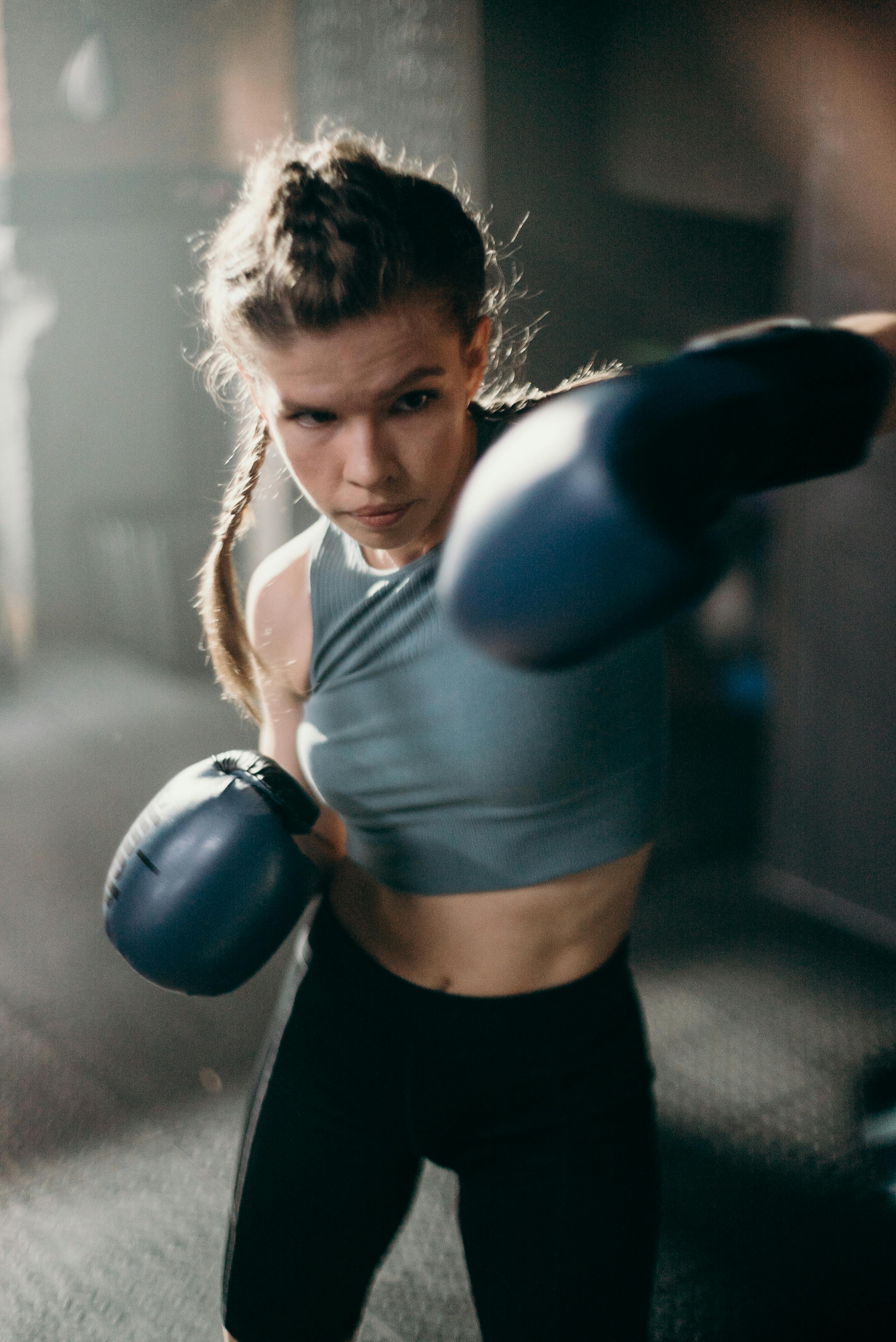 A woman in boxing gloves mid-strike, photographed in low natural light.