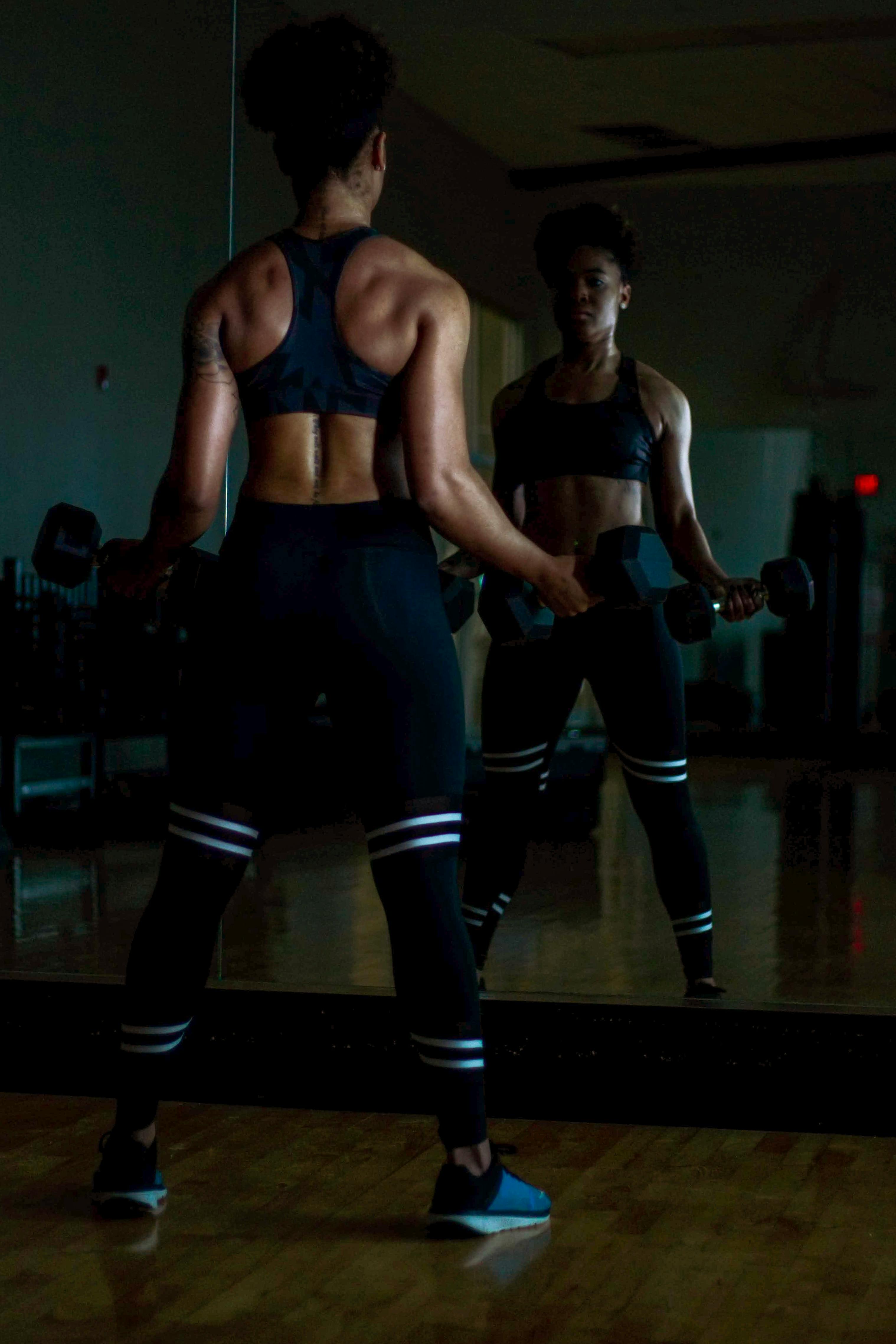 A woman lifting in a dim mirrored studio — quiet strength.